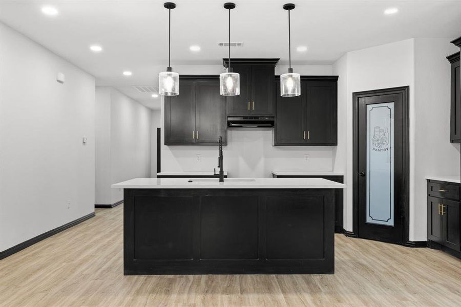 Kitchen with pendant lighting, light wood-type flooring, and a center island with sink