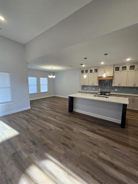 Kitchen featuring dark wood-type flooring, pendant lighting, and a center island with sink