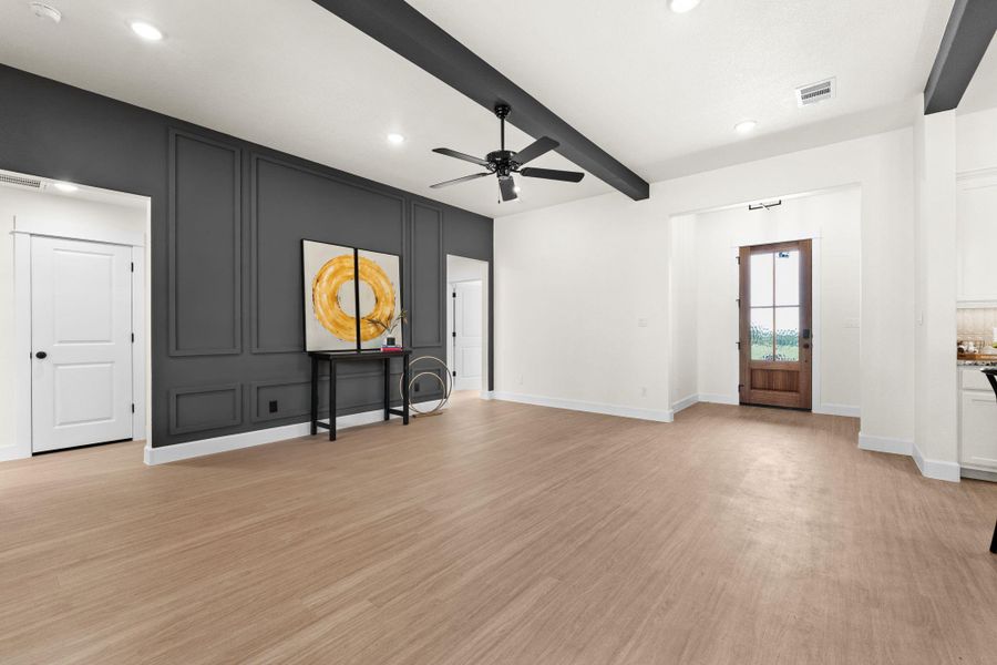 Unfurnished living room with ceiling fan, beam ceiling, light wood-style flooring, a decorative wall, and recessed lighting