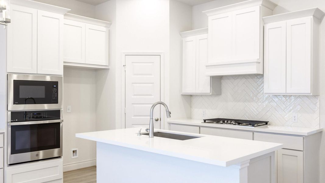 Kitchen with stainless steel appliances, a sink, backsplash, white cabinetry, and a kitchen island with sink Kitchen with stainless steel appliances, a sink, backsplash, white cabinetry, and a kitchen island with sink