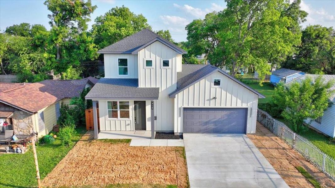 Modern two-story residence featuring board and batten siding, a dark gray shingled roof, an attached two-car garage, a covered entry porch with square columns, and a concrete driveway Modern two-story residence featuring board and batten siding, a dark gray shingled roof, an attached two-car garage, a covered entry porch with square columns, and a concrete driveway
