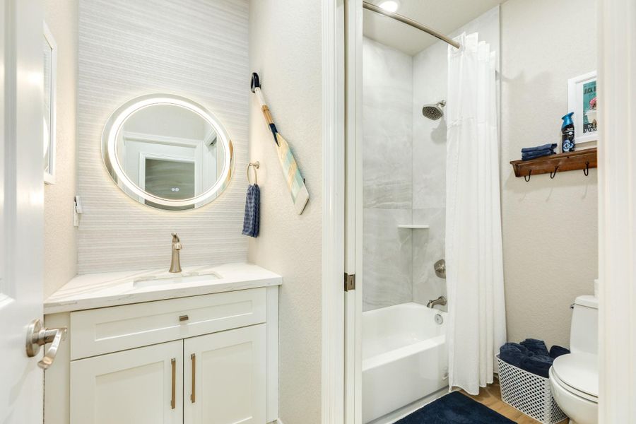 Well-appointed guest bathroom includes a quartz vanity, designer lighting, and a tub/shower combination with contemporary tile surround.