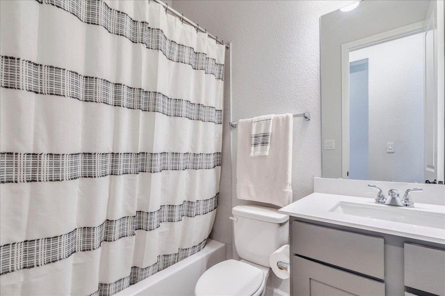 Bathroom featuring a textured wall, vanity, and shower / bathtub combination with curtain