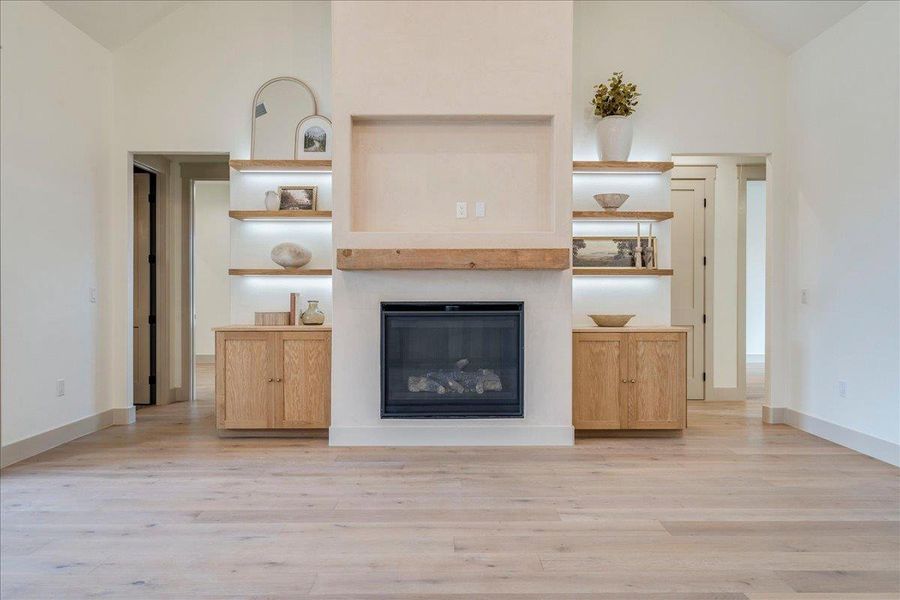 A well-lit living space features built-in shelving, a natural wood mantel, and a sleek fireplace.