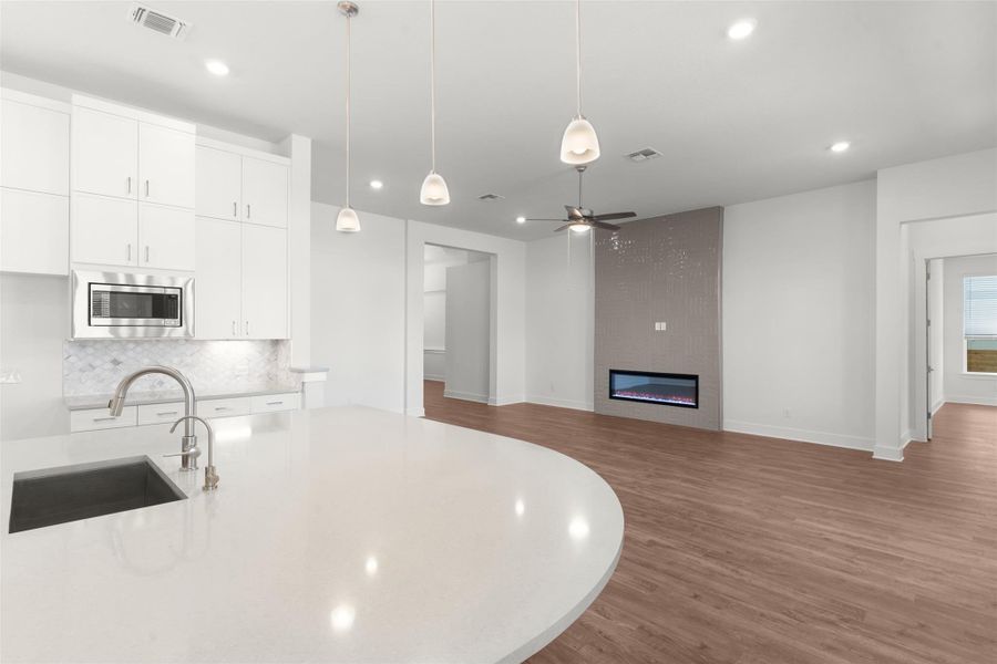 Kitchen with backsplash, dark wood-style flooring, white cabinetry, hanging light fixtures, and a large fireplace