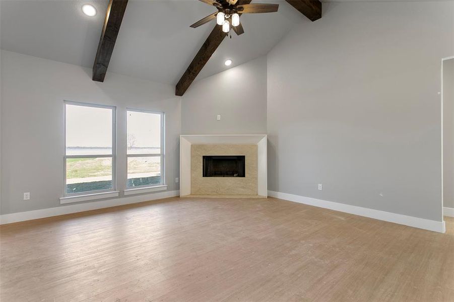 Unfurnished living room featuring beam ceiling, a fireplace, ceiling fan, and light hardwood / wood-style flooring