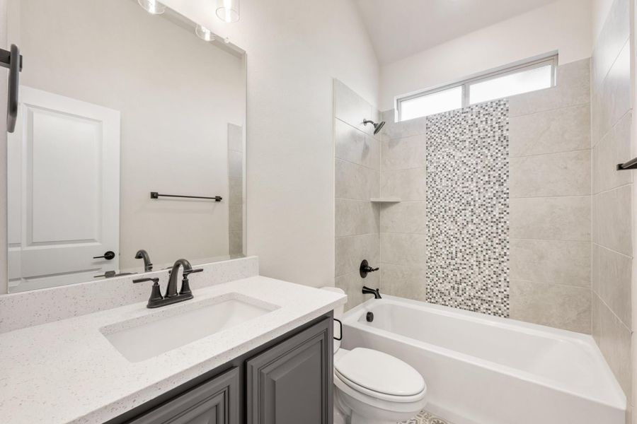 Bathroom with gray vanity, quartz countertop, and tiled tub-shower combo with mosaic accent strip Bathroom with gray vanity, quartz countertop, and tiled tub-shower combo with mosaic accent strip