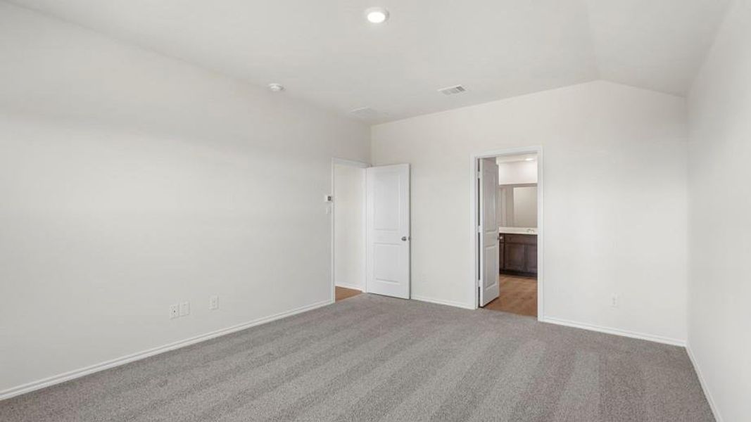 Spacious room featuring light gray carpet flooring, white painted walls, and a vaulted ceiling with a recessed light fixture