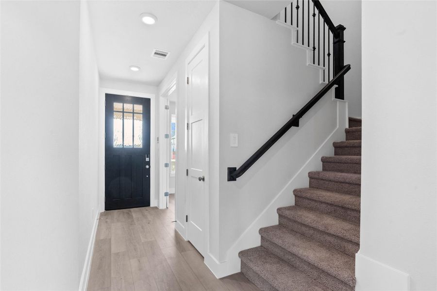 The staircase features a bold contrast of bright white risers and stringers against a striking matte black handrail, newel post, and iron balusters. The staircase features a bold contrast of bright white risers and stringers against a striking matte black handrail, newel post, and iron balusters.