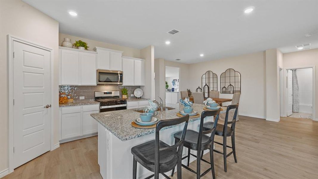 Kitchen featuring a kitchen breakfast bar, white cabinets, stainless steel appliances, light wood-style flooring, and recessed lighting Kitchen featuring a kitchen breakfast bar, white cabinets, stainless steel appliances, light wood-style flooring, and recessed lighting