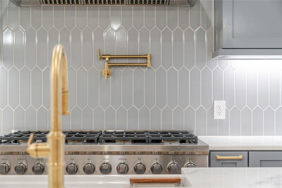 Kitchen view of slate blue cabinets, stainless steel gas cooktop, tasteful backsplash, exhaust hood, and light stone countertops