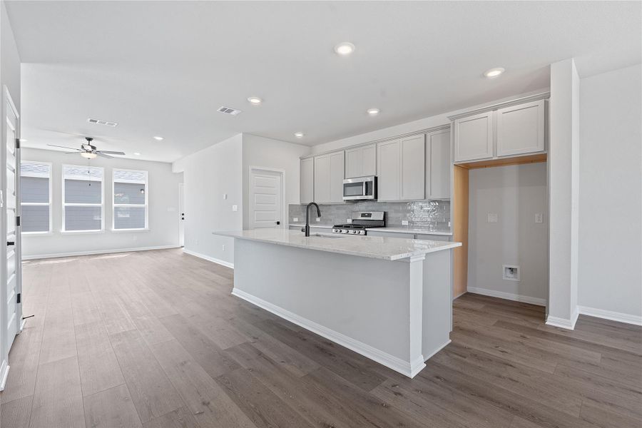 Kitchen featuring wood finished floors, tasteful backsplash, a ceiling fan, stainless steel appliances, and a center island with sink
