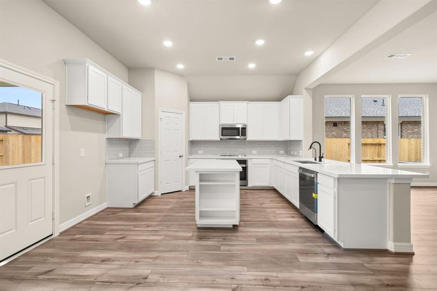 This light and bright kitchen features a large quartz island, white cabinets, a large sink overlooking your family room, recessed lighting, and beautiful backsplash.