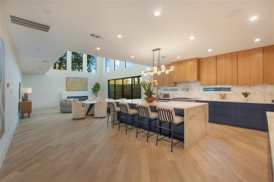 Kitchen with a breakfast bar, a kitchen island with sink, sink, light hardwood / wood-style flooring, and light stone countertops