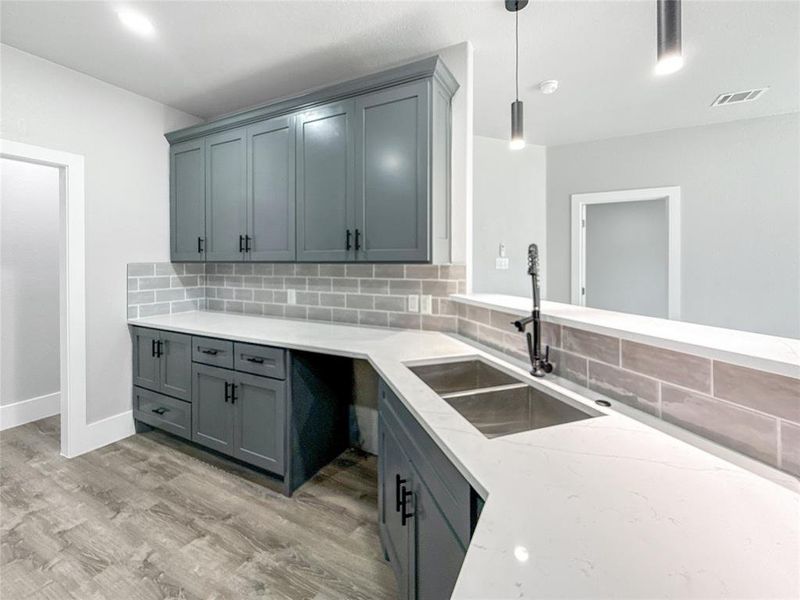 Kitchen with decorative backsplash, gray cabinetry, light stone countertops, light wood-type flooring, and pendant lighting