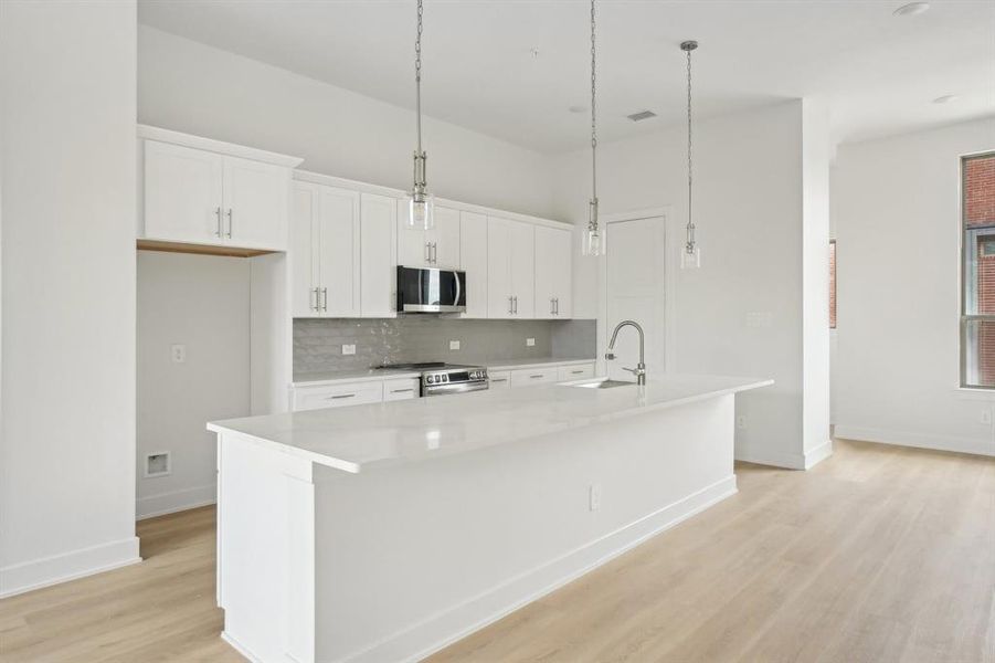 Kitchen with appliances with stainless steel finishes, a sink, a large island, light wood-type flooring, and tasteful backsplash