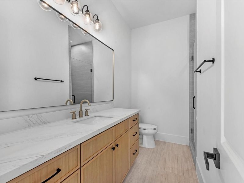 A rare downstairs secondary suite featuring a private en-suite bath with quartz vanity, abundant counter space, framed mirrors, designer lighting, and a spacious walk-in shower.