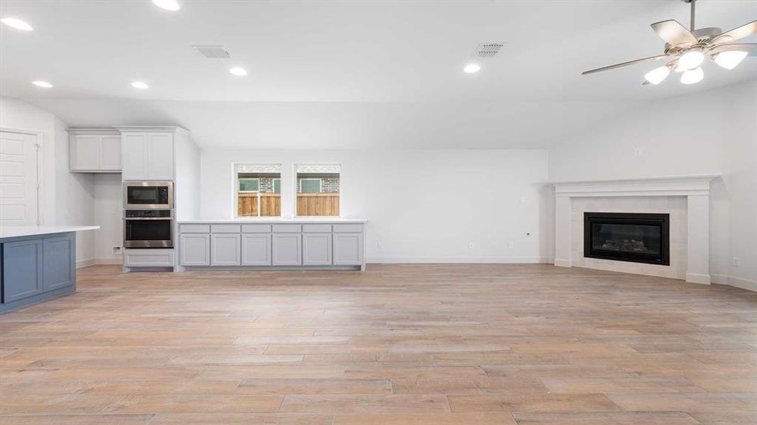 Unfurnished living room with a premium fireplace, light hardwood / wood-style flooring, ceiling fan, and lofted ceiling