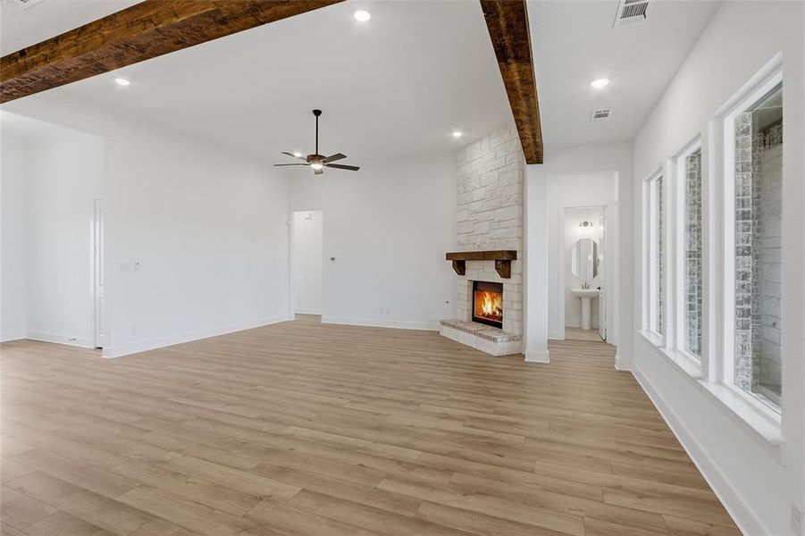 Unfurnished living room featuring beam ceiling, recessed lighting, a stone fireplace, ceiling fan, and light wood finished floors