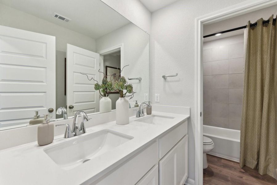 A spacious double vanity matches perfectly with the clean tiled tub surround and rich wood-style flooring.