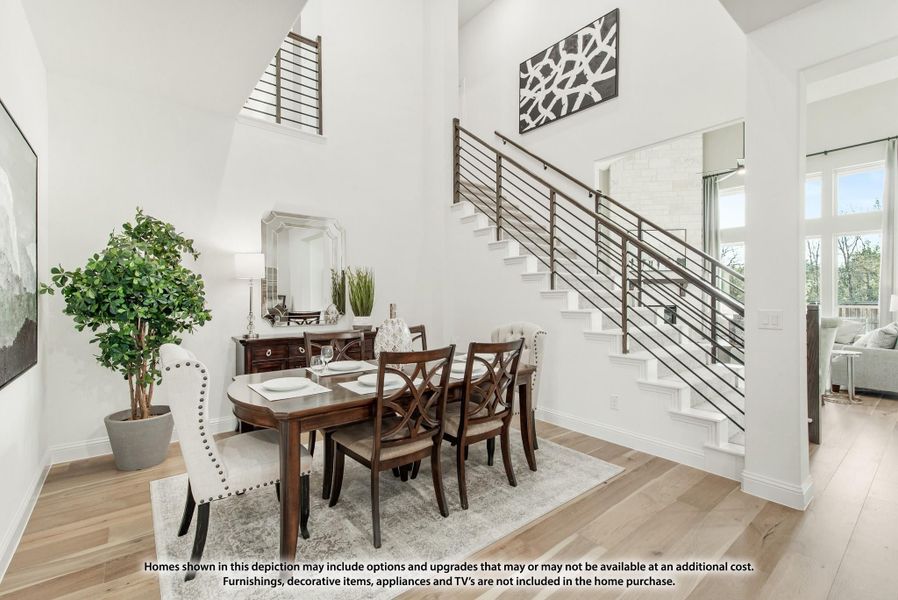Dining room with two-story ceiling, wood dining set, and staircase with metal railing and hardwood floors