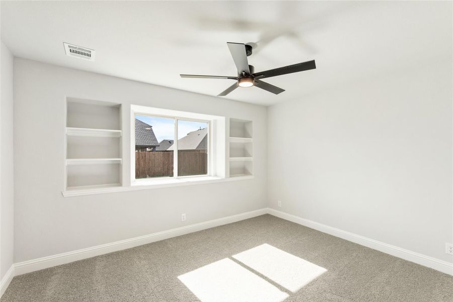 Empty bedroom with built-in shelves, ceiling fan, carpet flooring, and a single window