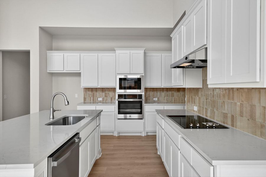 Kitchen with appliances with stainless steel finishes, an island with sink, white cabinetry, light wood finished floors, and light stone counters Kitchen with appliances with stainless steel finishes, an island with sink, white cabinetry, light wood finished floors, and light stone counters