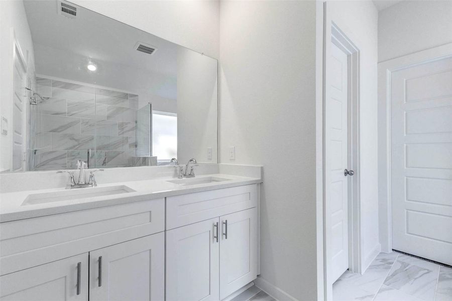 Primary bath vanity with dual sinks, white cabinetry, chrome fixtures, large mirror, and access to the private bath areas. The neutral finishes and thoughtful layout offer both function and style for everyday routines.