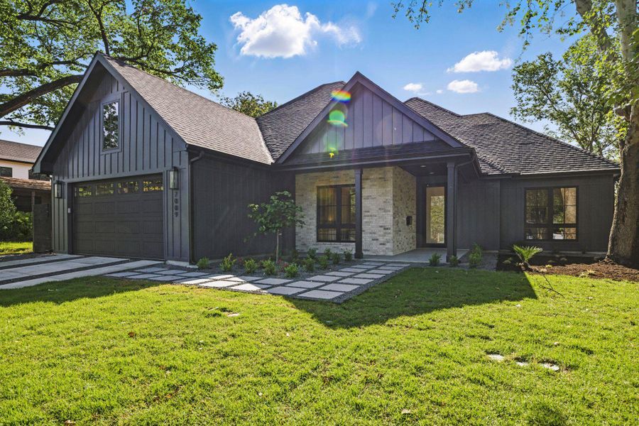 View of front facade with a front yard, roof with shingles, driveway, and board and batten siding