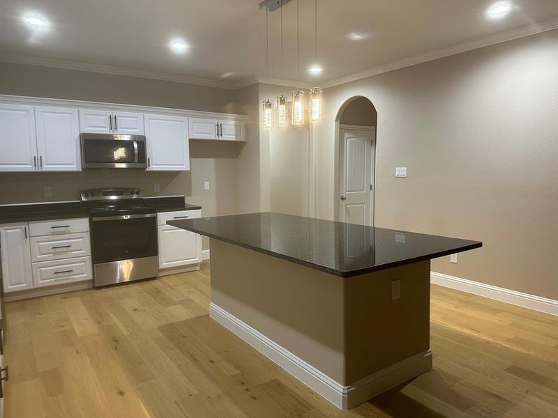 Kitchen with pendant lighting, light wood-type flooring, a center island, white cabinets, and appliances with stainless steel finishes