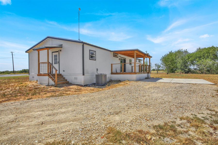 A gravel driveway leads to this single-level home featuring a covered deck and concrete patio.
