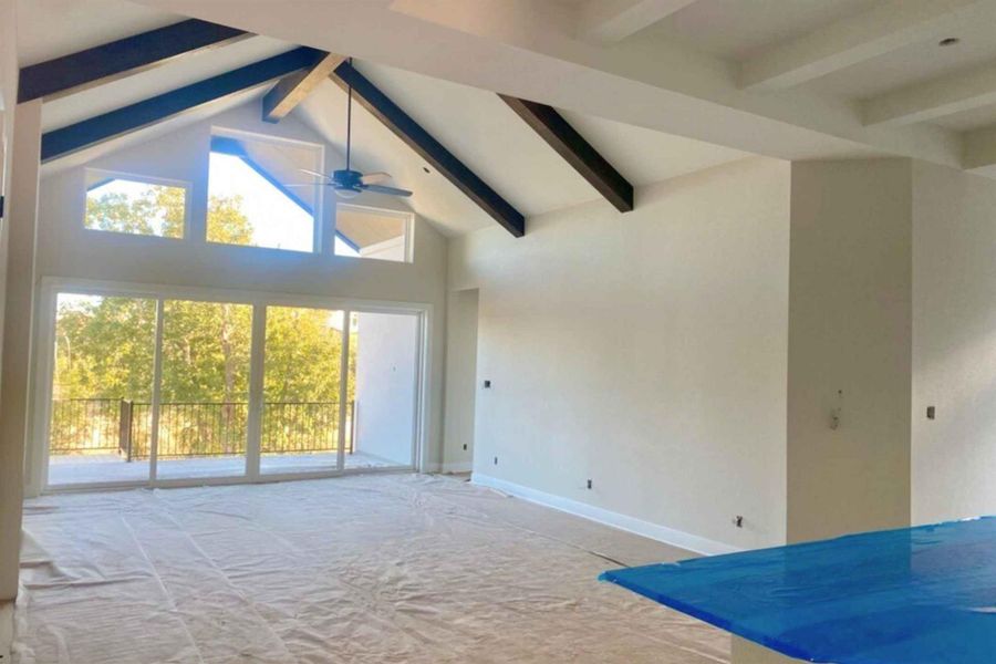 Unfurnished living room featuring high vaulted ceiling, beam ceiling, carpet floors, and a ceiling fan
