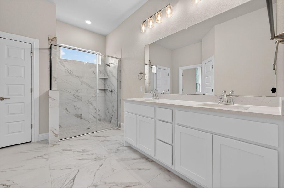 Bathroom with double vanity, light marble finish flooring, and a marble finish shower