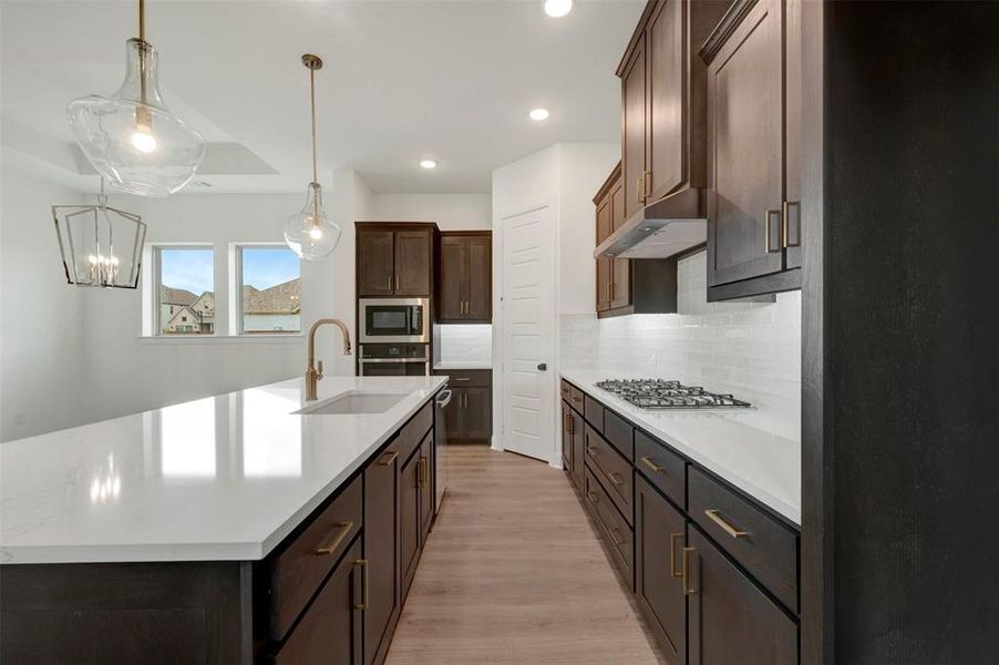 Spacious kitchen featuring a large central island with an undermount sink, brass faucet, and pendant lighting