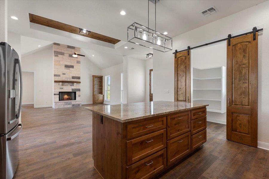 Kitchen featuring stainless steel refrigerator with ice dispenser, a barn door, light stone countertops, lofted ceiling, and dark wood-style flooring