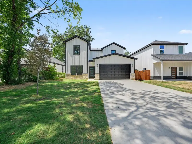Modern farmhouse-style exterior featuring vertical white siding, black trim accents, a two-car garage with a textured door, a concrete driveway, and a stone foundation detail Modern farmhouse-style exterior featuring vertical white siding, black trim accents, a two-car garage with a textured door, a concrete driveway, and a stone foundation detail