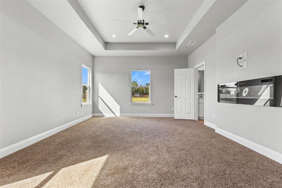 Carpeted empty room featuring a raised ceiling, recessed lighting, and a ceiling fan