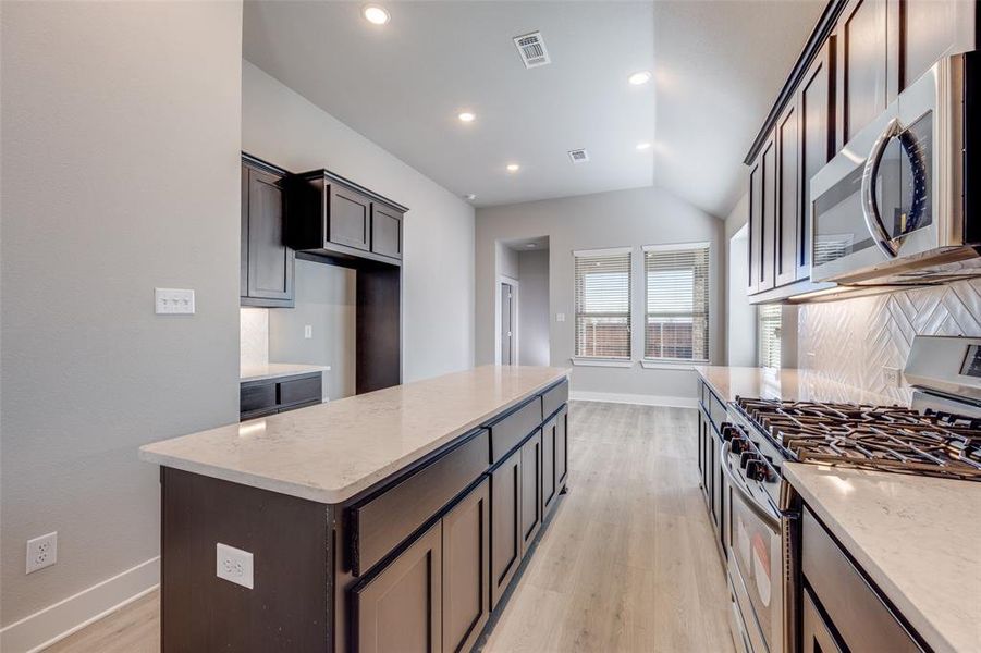 Kitchen featuring appliances with stainless steel finishes, a center island, light stone countertops, light wood-style floors, and recessed lighting