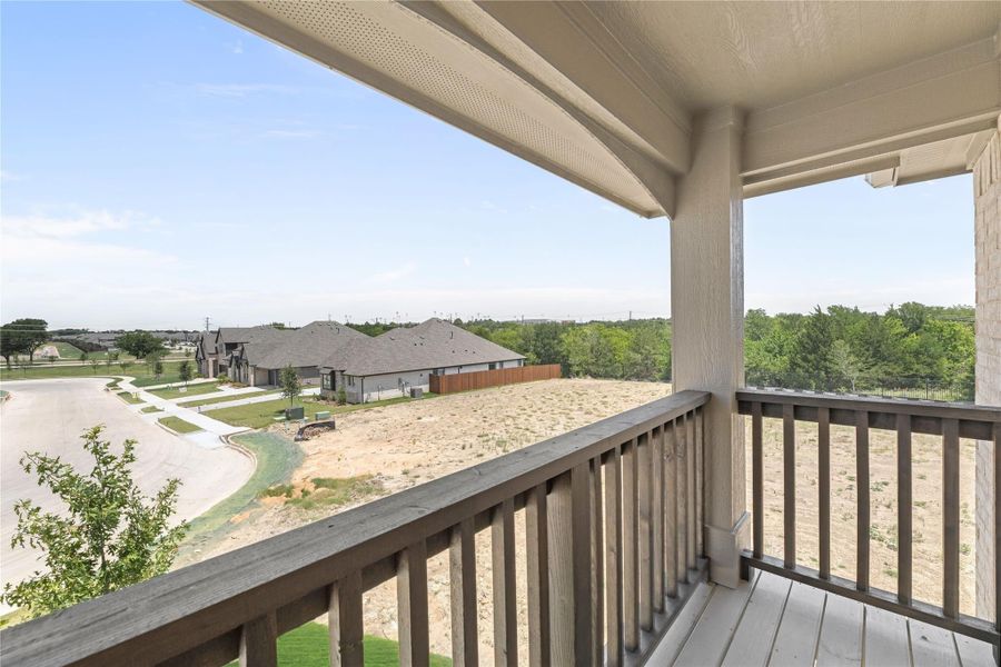 Covered balcony with wood railing overlooking a new subdivision and open land with trees in the distance
