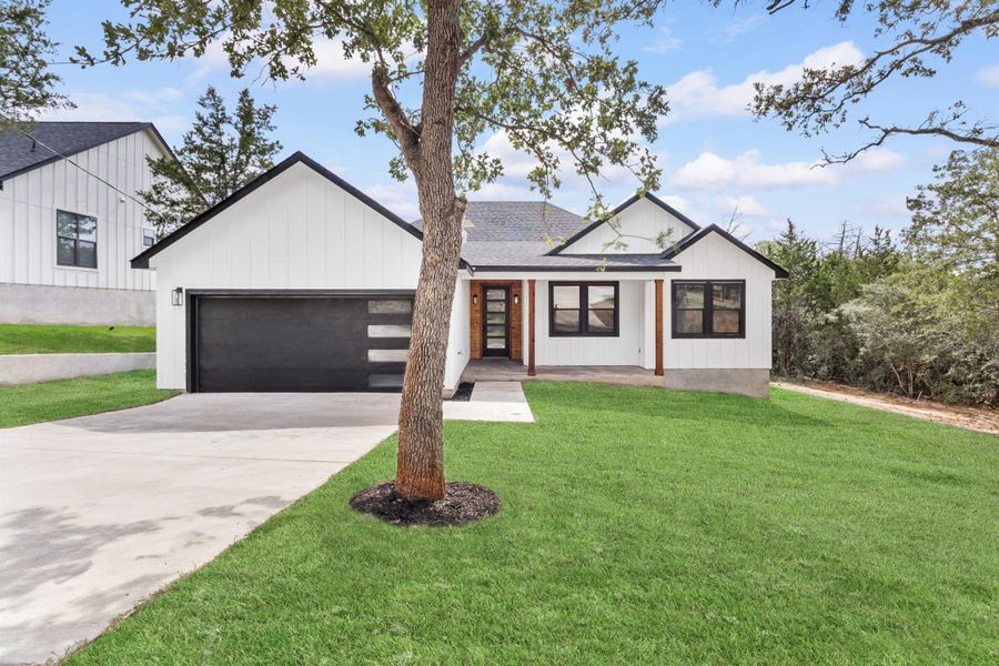 Modern inspired farmhouse featuring a front yard, concrete driveway, a porch, a shingled roof, and a garage