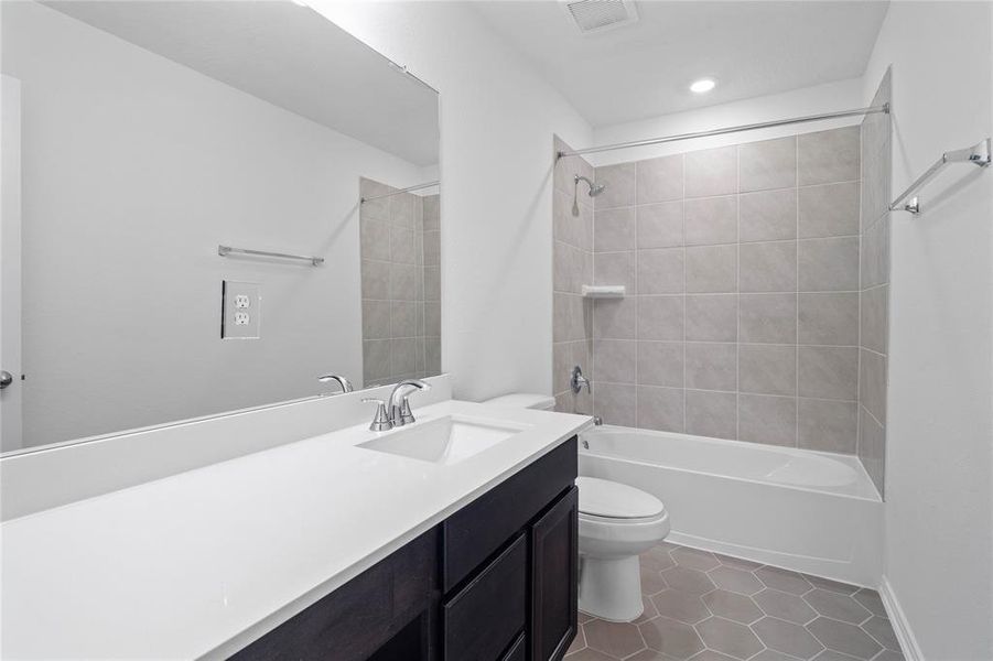 Secondary bath features tile flooring, tub/shower combo with tile surround, stained wood cabinets, beautiful light countertops, mirror, sleek fixtures and modern finishes.