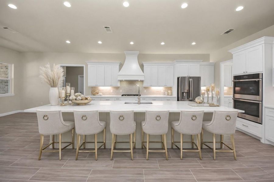 This modern kitchen boasts a spacious island with enough room for six, plus sleek white custom cabinetry, all stainless-steel appliances, and ample lighting, creating a bright and inviting space for entertaining.