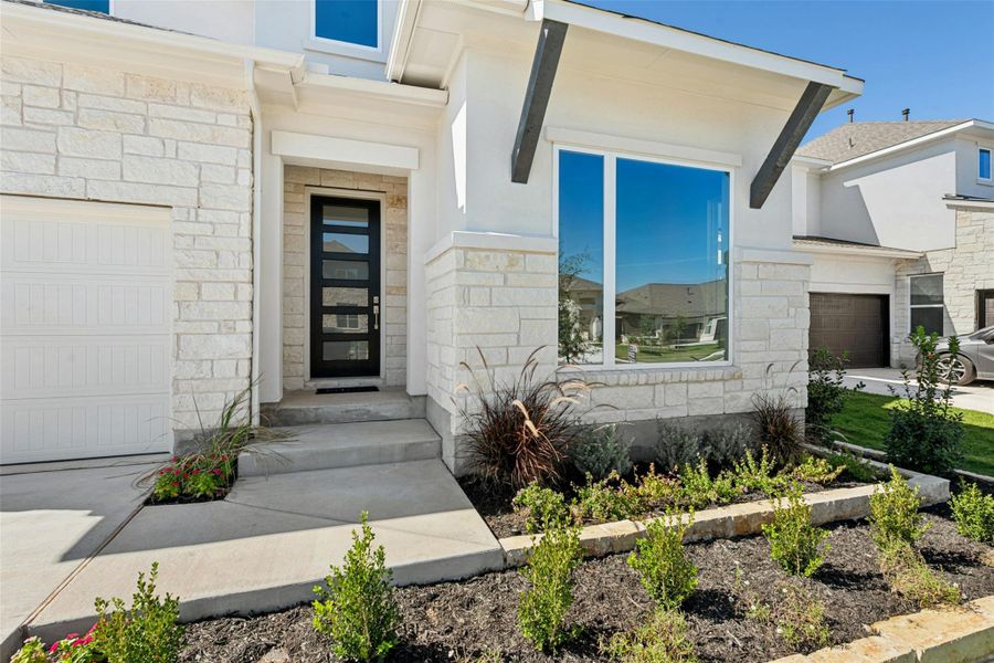 View of exterior entry featuring stone siding, an attached garage, and driveway