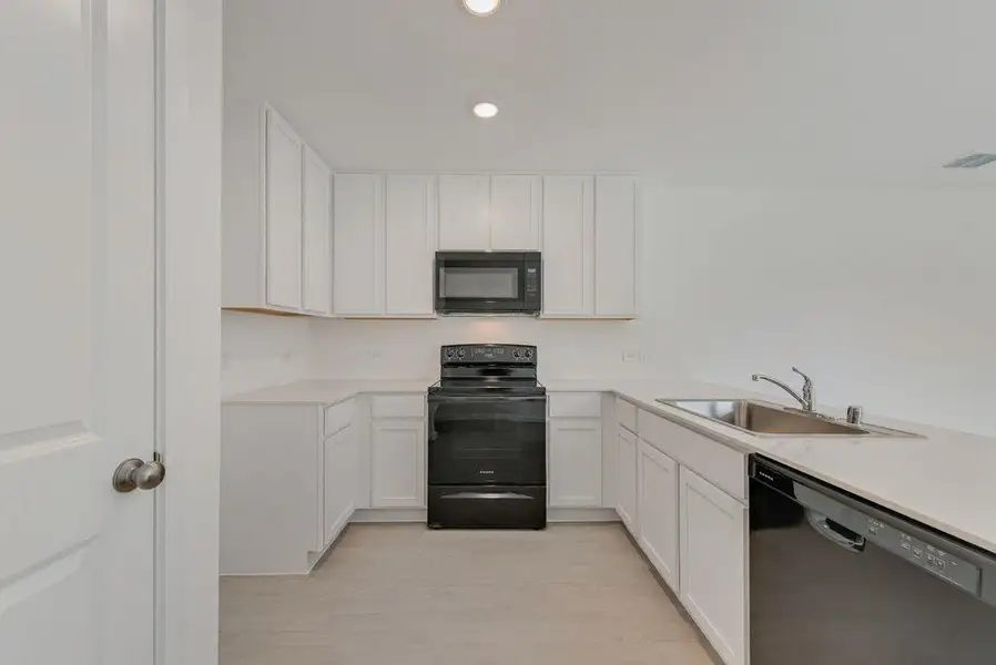 Kitchen with black appliances, light countertops, white cabinets, and recessed lighting