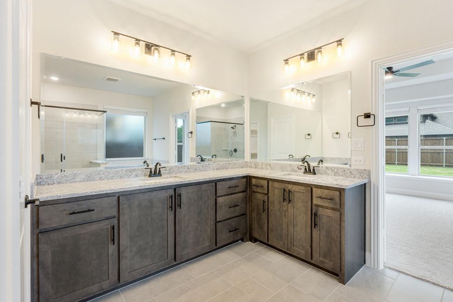 Master bathroom with L-shaped double vanity, dark wood cabinets, granite countertops, and large mirrors with overhead lighting. Master bathroom with L-shaped double vanity, dark wood cabinets, granite countertops, and large mirrors with overhead lighting.