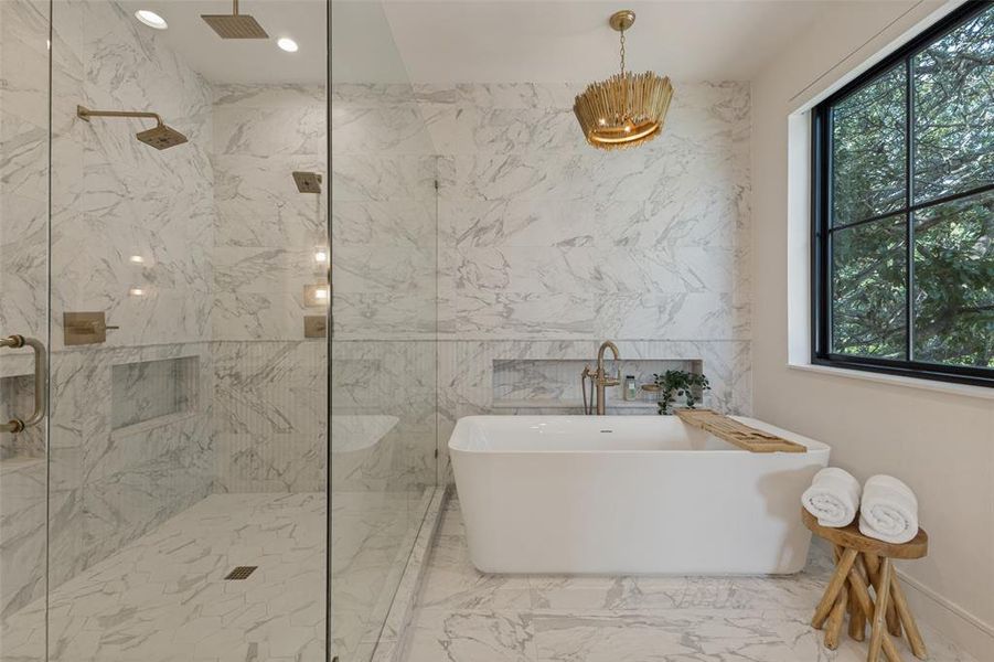 Freestanding soaking tub with gold-tone fixtures, surrounded by marble-patterned tile flooring and walls Freestanding soaking tub with gold-tone fixtures, surrounded by marble-patterned tile flooring and walls