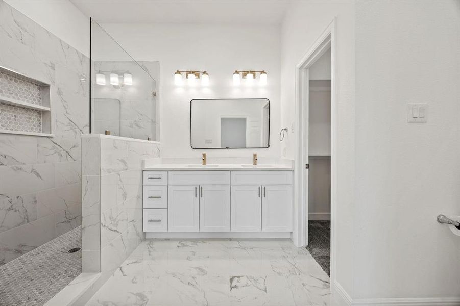 Spacious bathroom featuring marble-look tile flooring, a dual vanity with white cabinetry and gold-tone fixtures, and a glass-enclosed shower with a built-in niche and mosaic tile floor Spacious bathroom featuring marble-look tile flooring, a dual vanity with white cabinetry and gold-tone fixtures, and a glass-enclosed shower with a built-in niche and mosaic tile floor