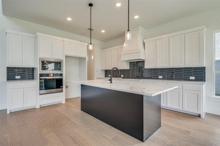 Kitchen with black microwave, stainless steel oven, decorative backsplash, and light hardwood / wood-style floors