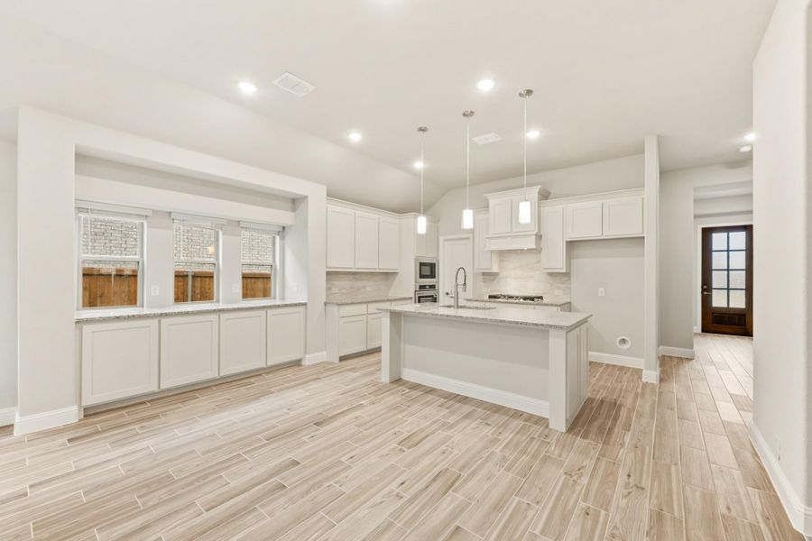 Open kitchen with white cabinets, center island, granite countertops, and light wood-look tile floors Open kitchen with white cabinets, center island, granite countertops, and light wood-look tile floors