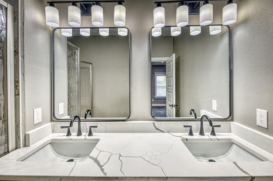 Bathroom featuring a textured wall, double vanity, and a shower stall